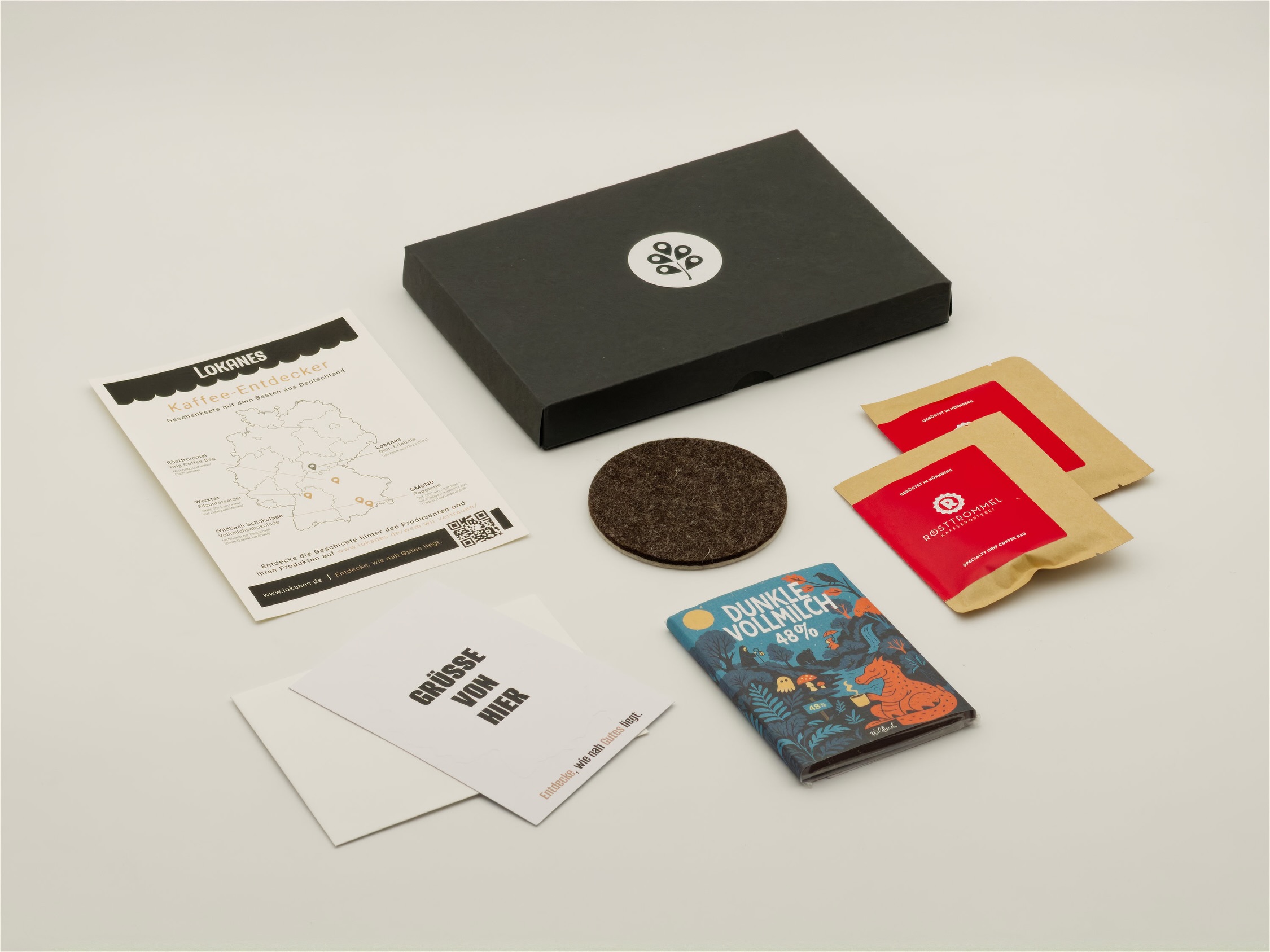 Geöffnete Entdeckerpost Kaffee mit Kaffeebeuteln, Schokolade, Filzuntersetzer, Grußkarten und Flyer