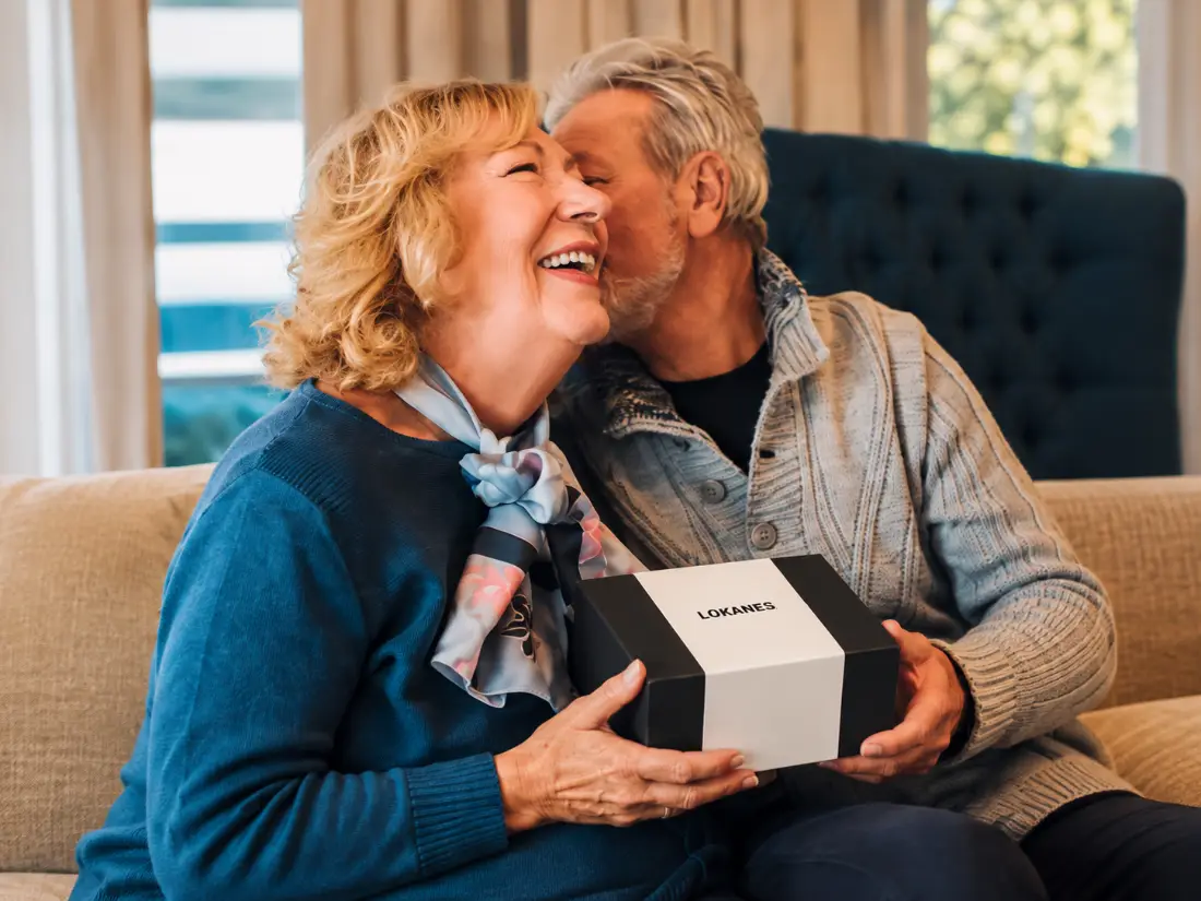 Älteres Paar mit einer LOKANES-Geschenkbox bei einem liebevollen Moment auf dem Sofa
